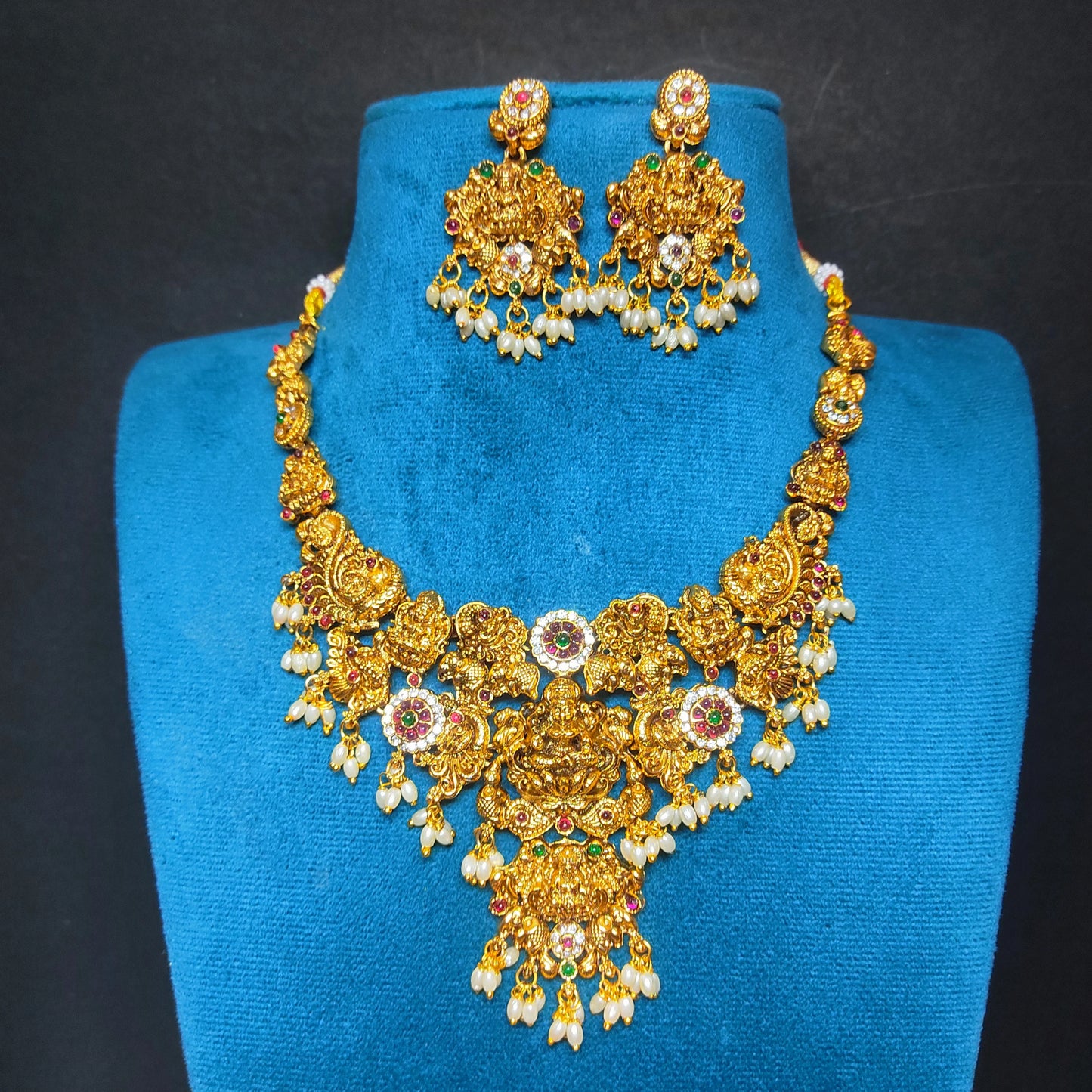 Antique gold finish bridal necklace and earrings set on a blue mannequin against a dark background