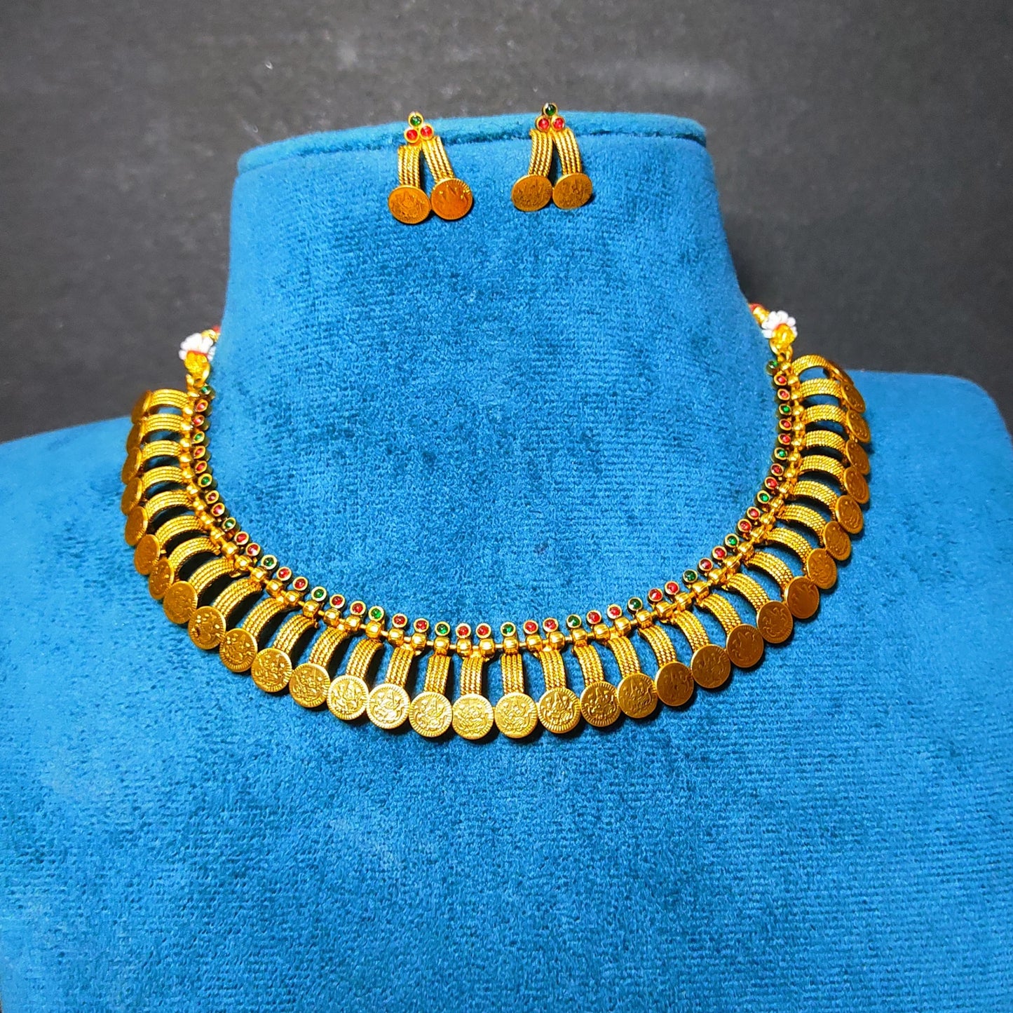 Antique Gold Finish coin necklace and matching drop earrings displayed on a blue velvet jewelry bust against a dark gray background.
