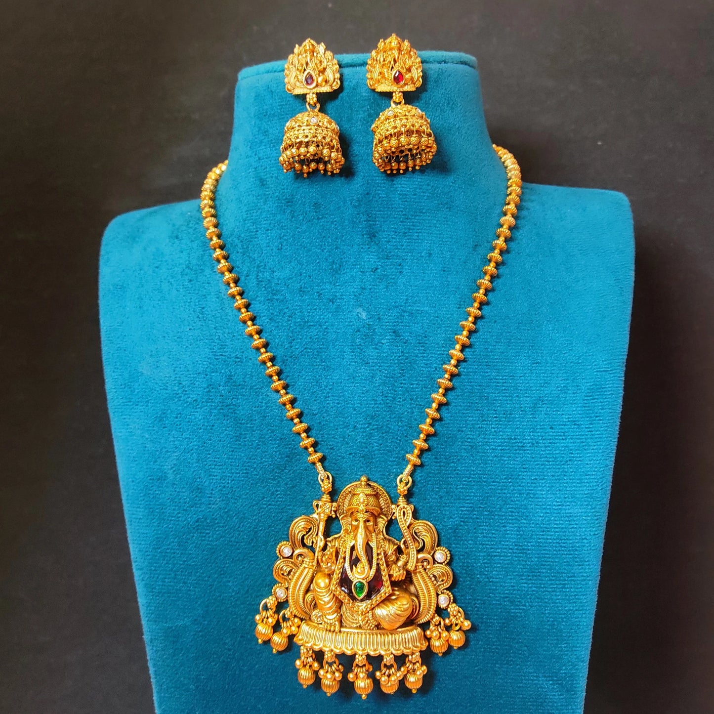 Traditional Indian matte antique gold temple necklace featuring a Lord Ganesha pendant and matching Jhumka earrings on a blue mannequin