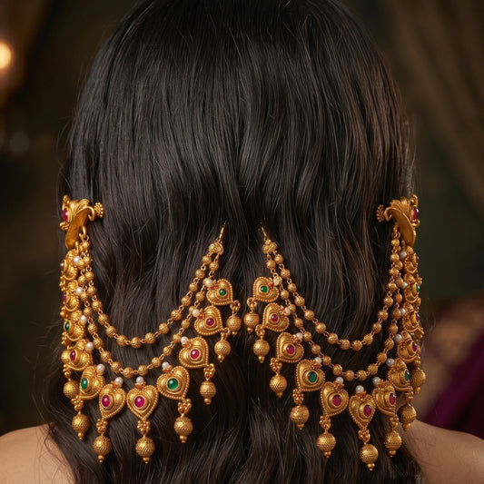 A pair of traditional Indian 3-layer antique gold mattal ear chains with ruby red and emerald green kemp stones, displayed beautifully as a hair accessory