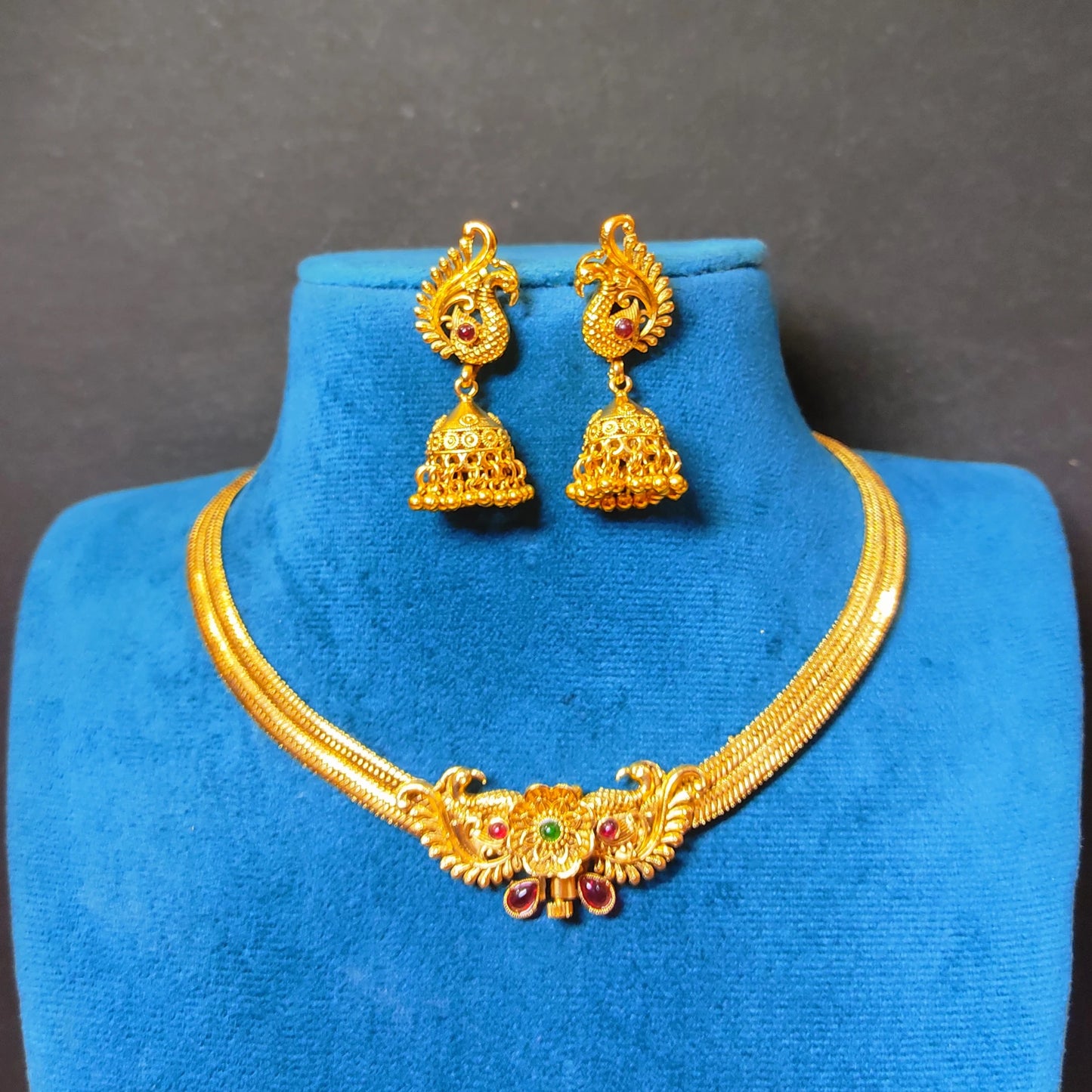 Traditional Indian temple jewelry set featuring a rigid gold peacock collar necklace and dangling Jhumkas in antique gold finish