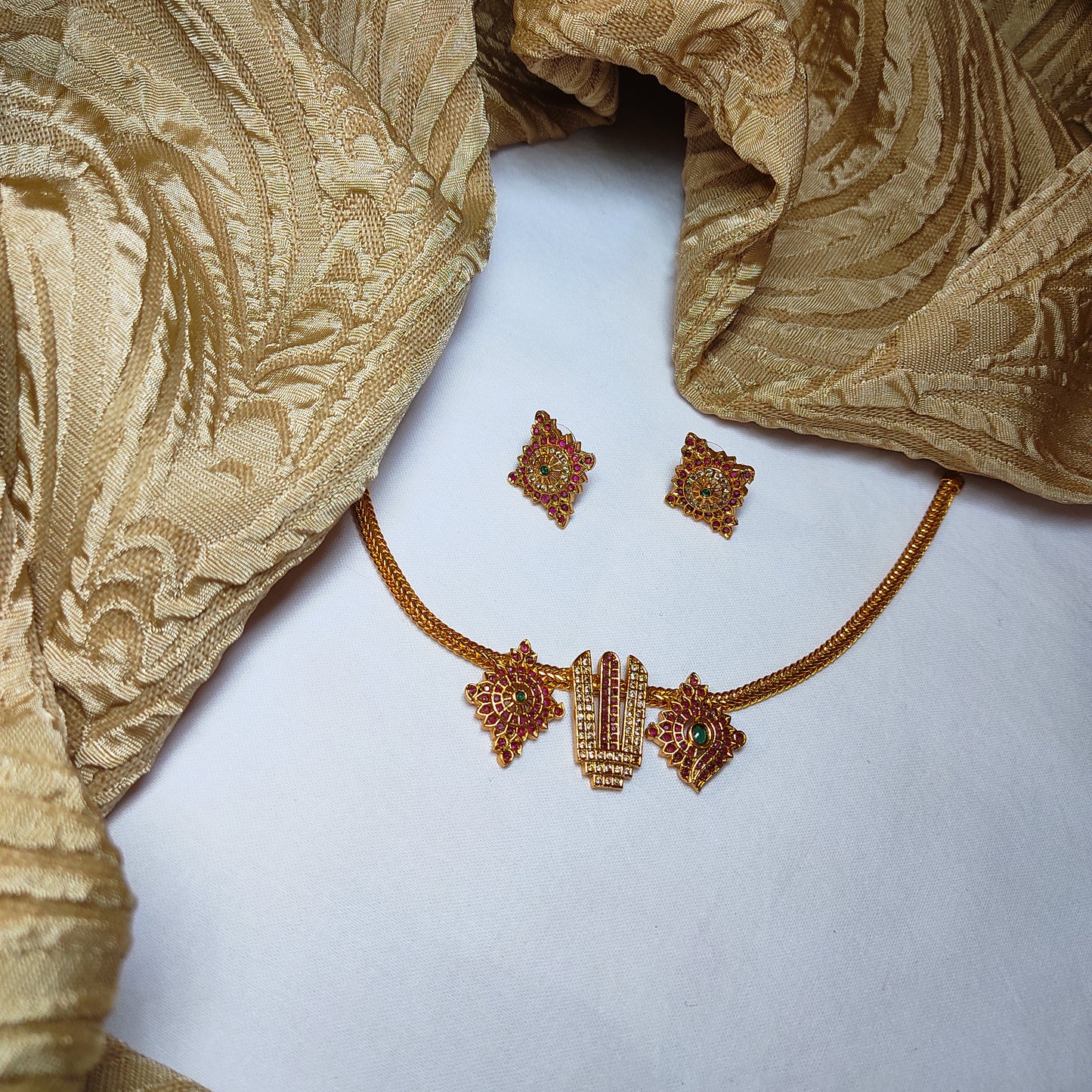 Gold toned necklace and earrings on a textured gold fabric background
