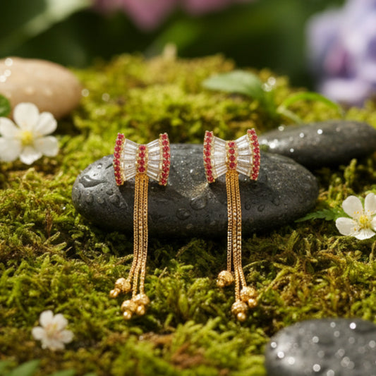 Pair of earrings with gold plated and red details on a mossy stone surface with flowers.