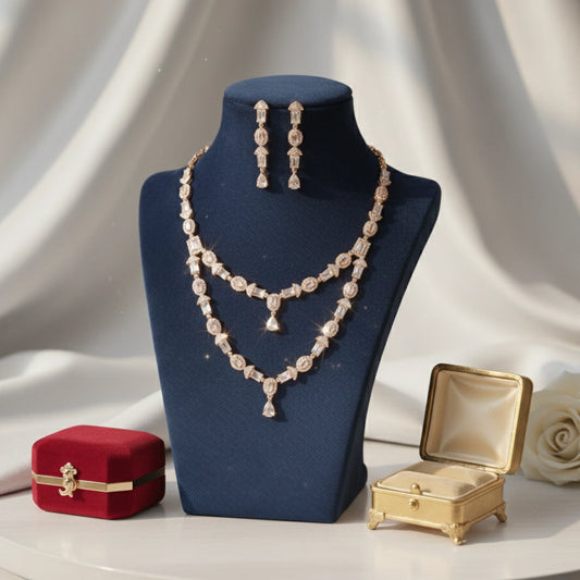 Jewelry set including a Rose Gold necklace and earrings on a blue mannequin bust with decorative boxes and a rose in the background.