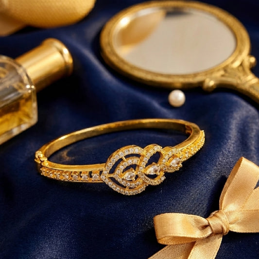 Gold plated bracelet with diamonds on a blue fabric background with a mirror, perfume bottle, and pearl.