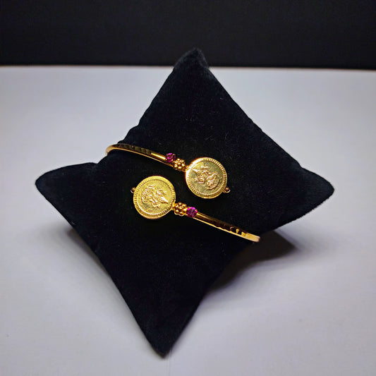 Gold plated bracelet with coin designs on a black pillow against a white background