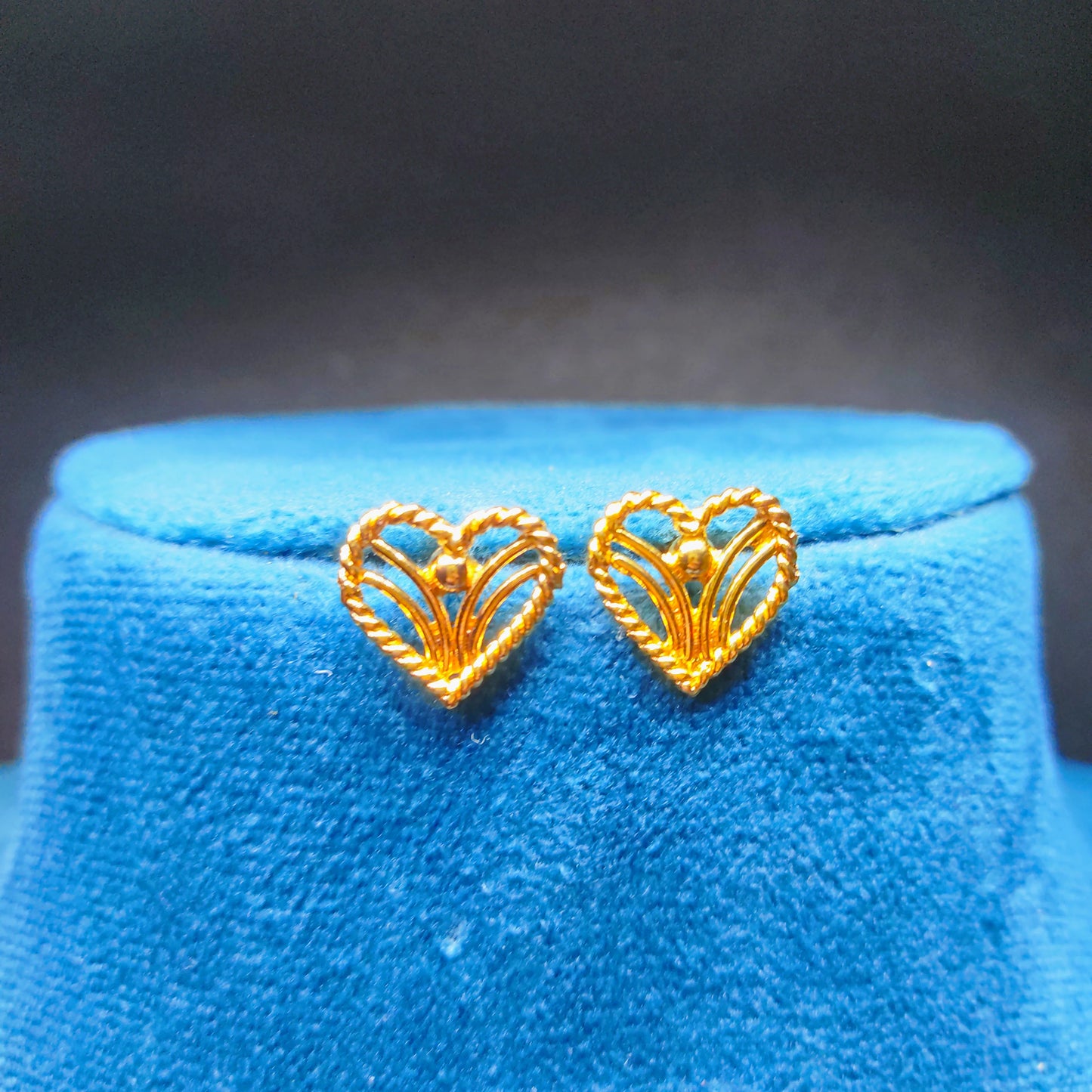 Gold plated heart-shaped earrings on a blue cushion with a dark background