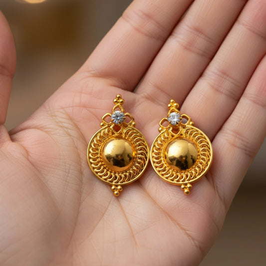 Gold plated Dome Stud earrings with intricate designs held in a hand against a blurred background