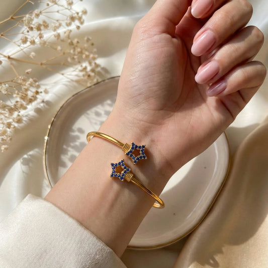 Gold plated bracelet with blue stones on a hand against a neutral background