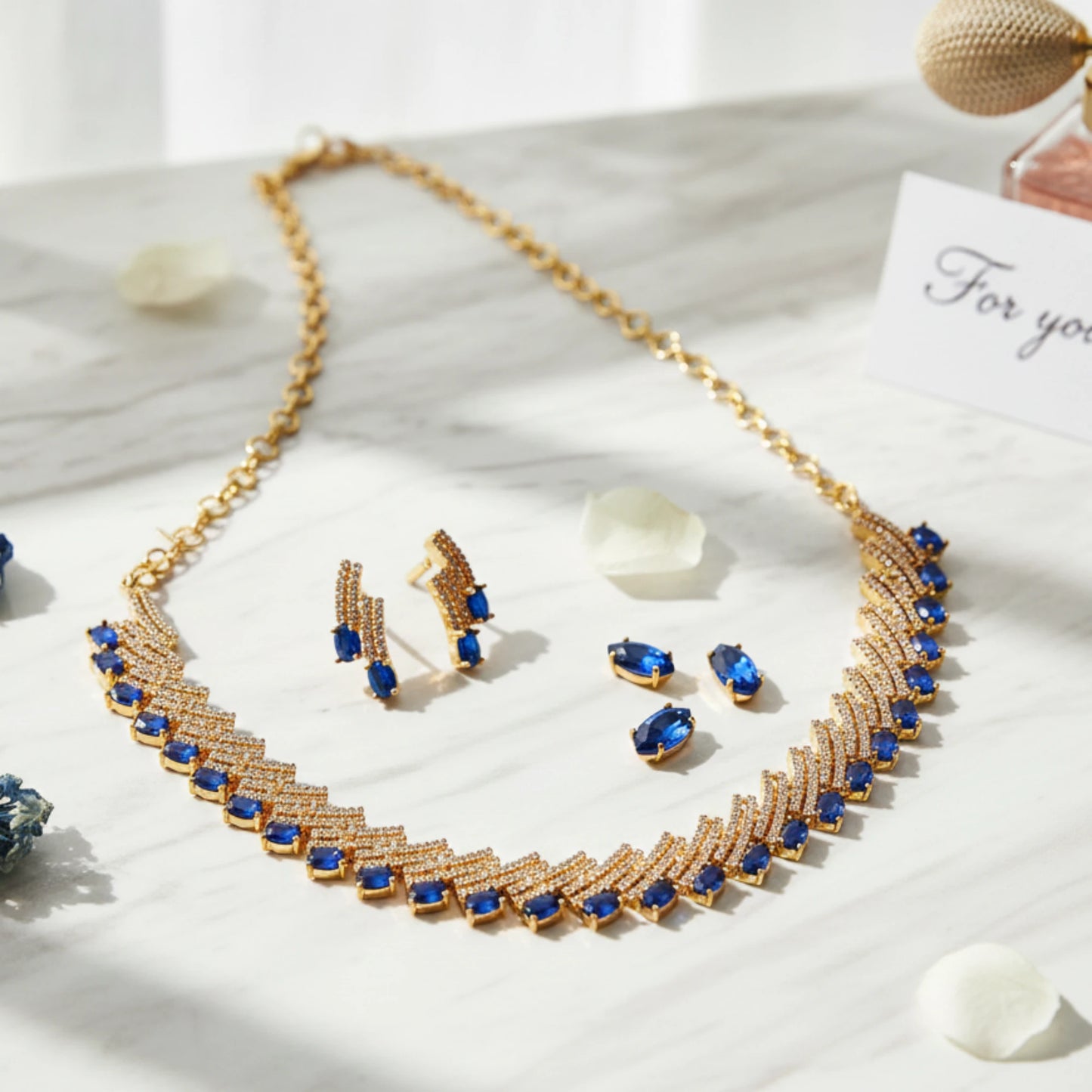 Gold plated necklace with white and blue ad stones and matching earrings on a white surface.