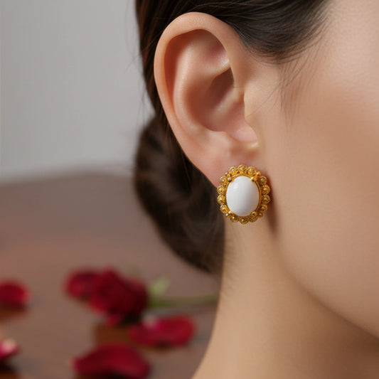 Close-up of a person wearing a gold plated earring with a oval center white stone, surrounded by red flowers.