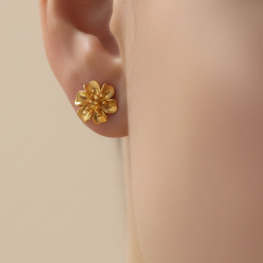 Gold plated flower-shaped earring on a person's ear against a beige background