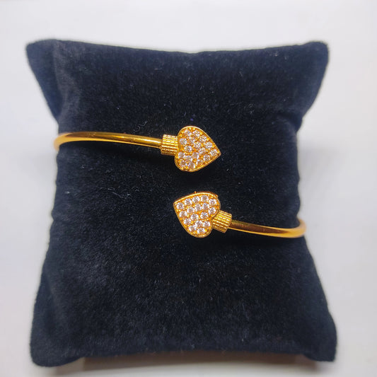 Gold plated heart-shaped bangle/cuff on a dark blue cushion