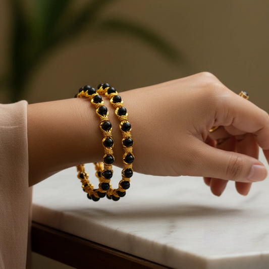 Hand wearing two gold plated karimani/ black beaded bangles on a neutral background
