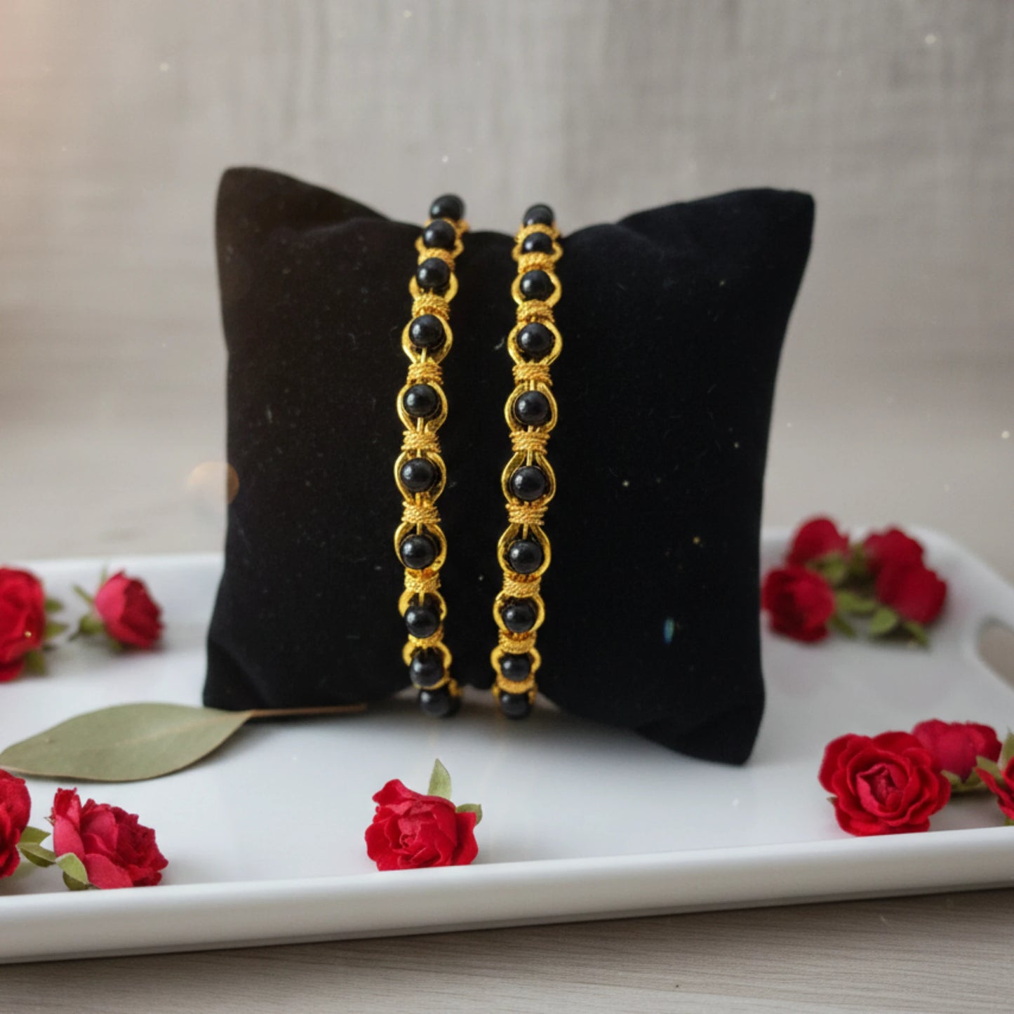 Pair of black bangles in karimani or black beaded on a black pillow with red roses around.