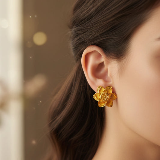 Gold plated flower earring worn by a person with a blurred background