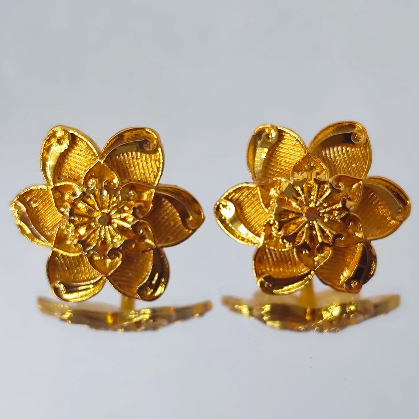 Pair of gold plated flower-shaped earrings on a light gray background