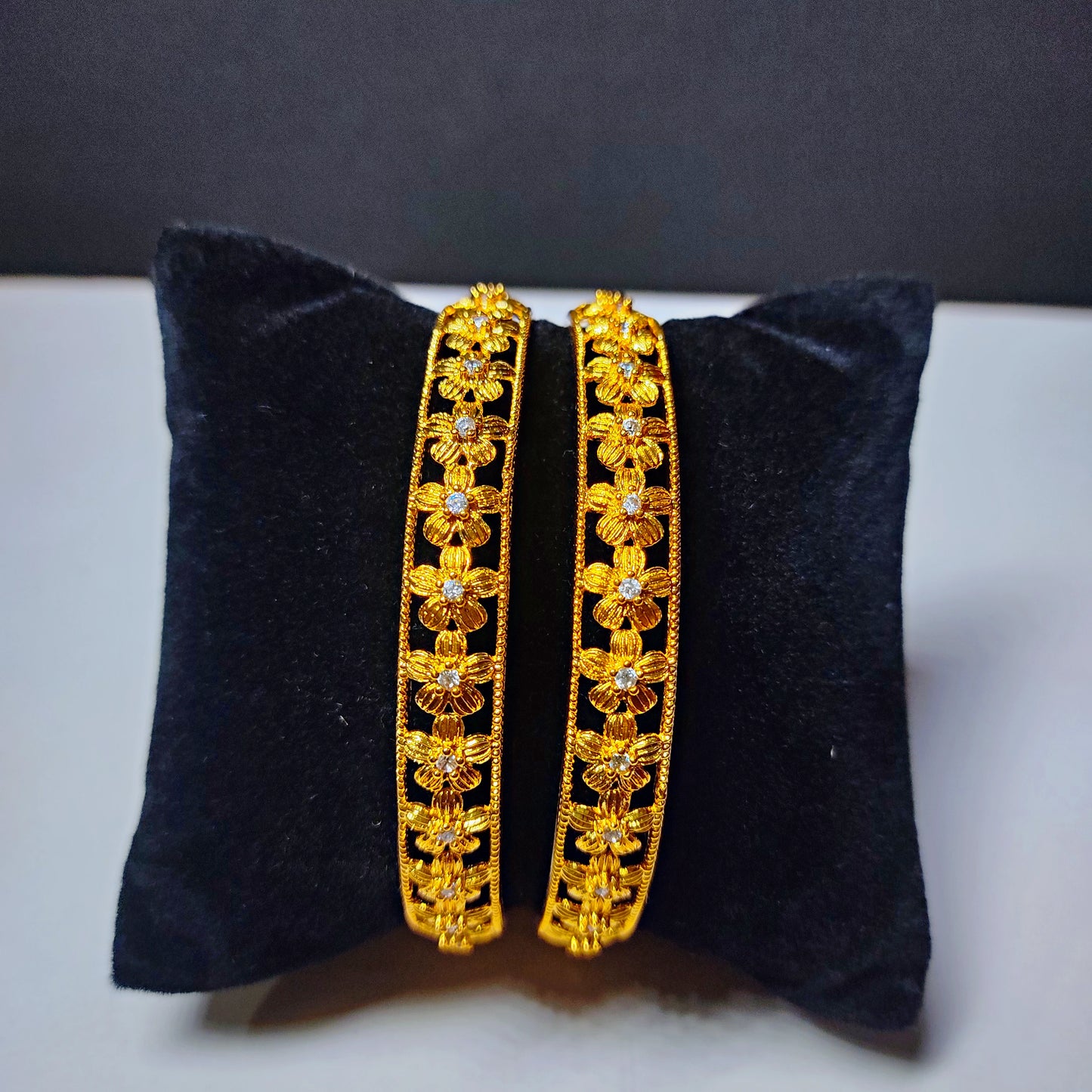 Pair of gold plated bangles on a black cushion with a dark background