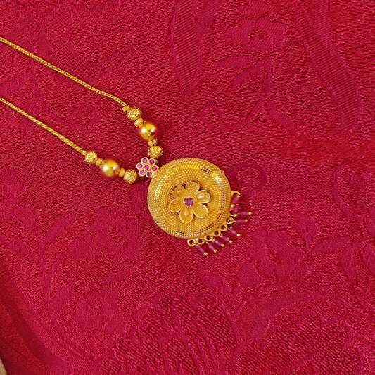 Gold plated necklace with a floral pendant on a red textured fabric background