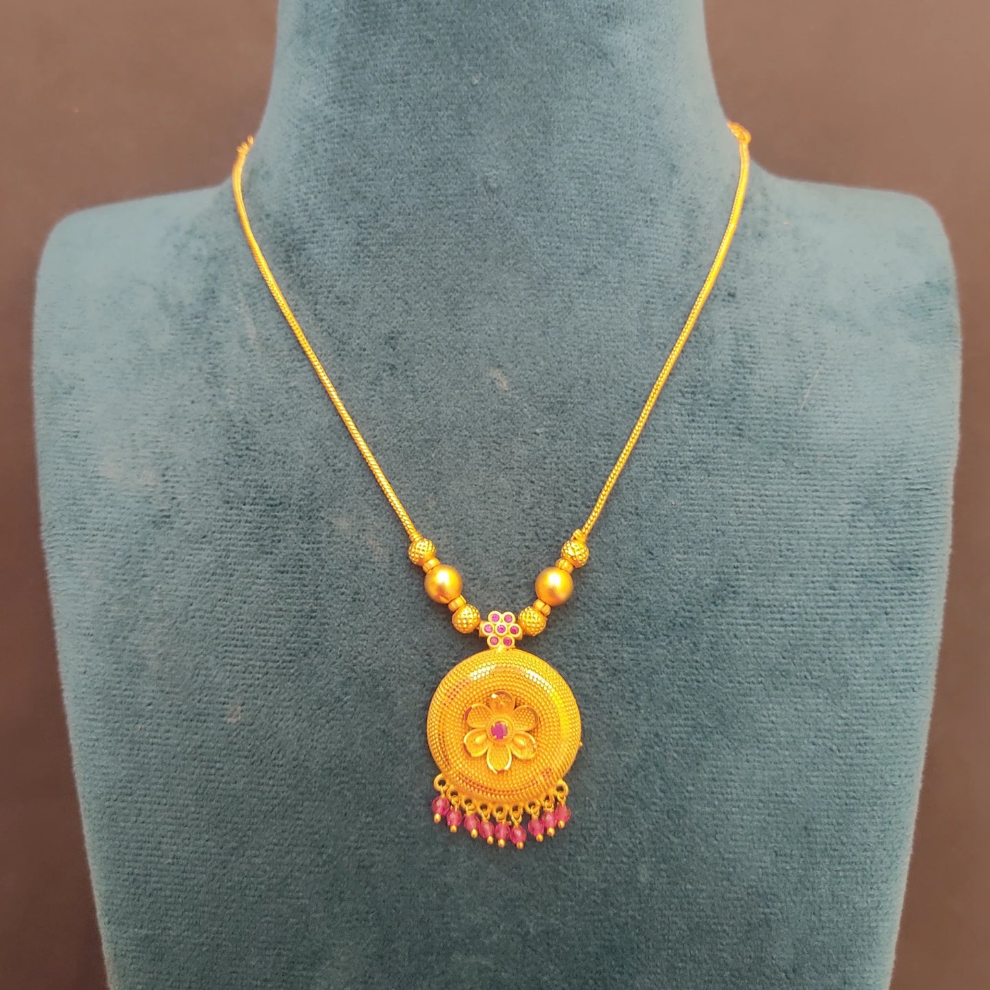 Gold Plated necklace with a floral pendant on a mannequin bust against a brown background