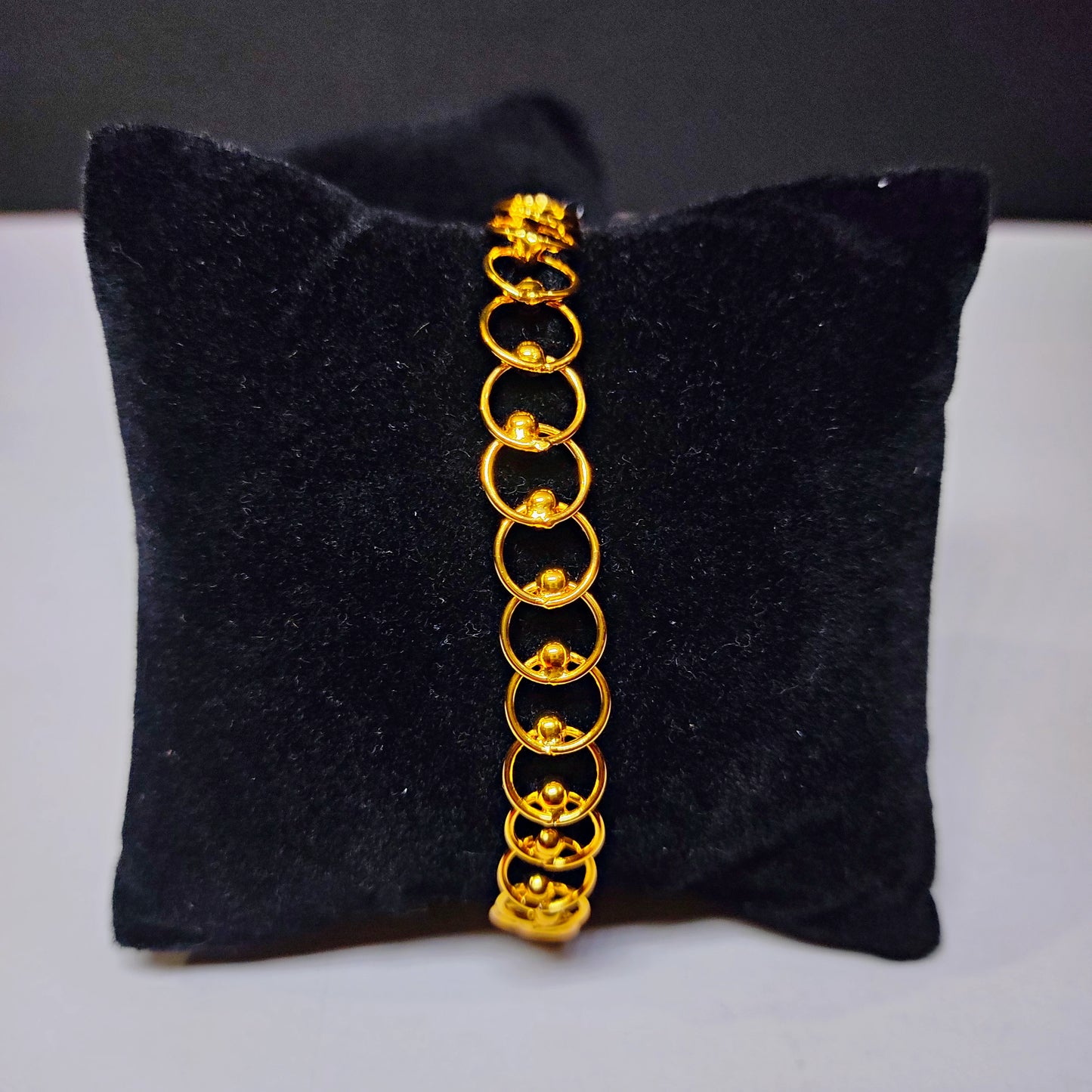 Gold plated bracelet on a black cushion with a gray background