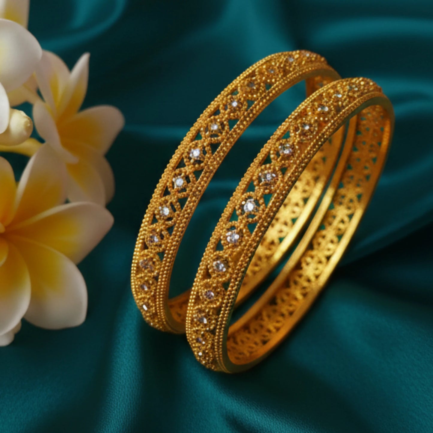 Gold plated bangles with intricate designs and AD accents on a teal fabric background with flowers.