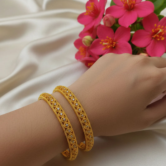 Gold plated bangles with AD accents in open work filigree pattern on a wrist with pink flowers in the background