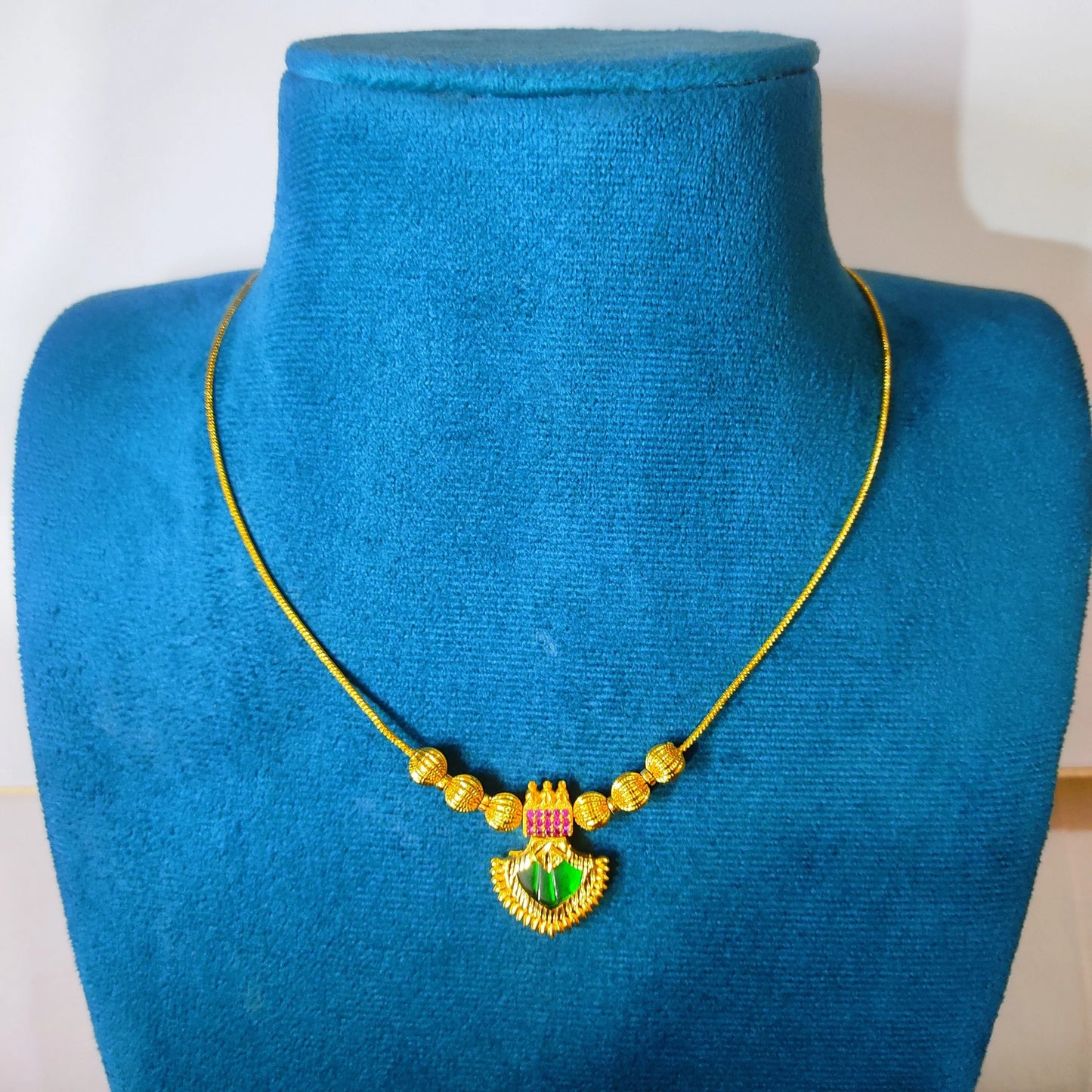Gold plated palakka necklace with a colorful pendant on a blue mannequin bust.
