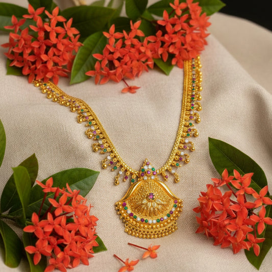 Gold plated Long Haram necklace with colorful stones and a pendant on a beige fabric background with red flowers and green leaves.