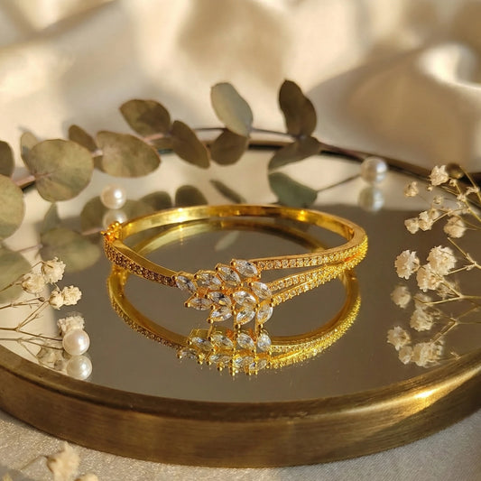 Gold plated bracelet with floral design on a reflective surface with leaves and flowers.