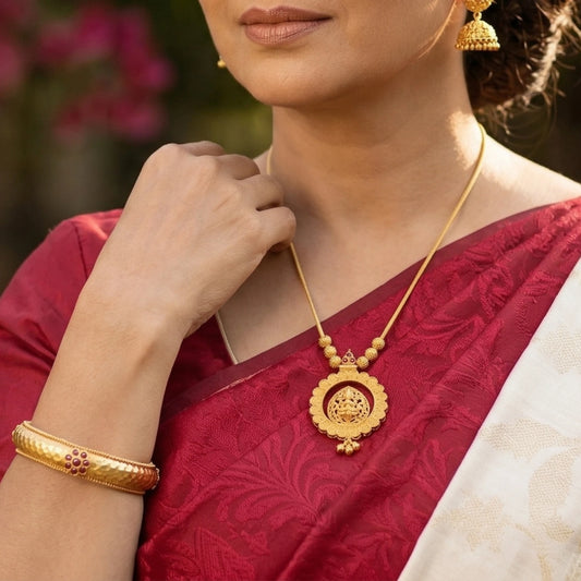 Woman wearing a gold plated necklace with matte finish Lakshmi on a lotus shaped pendant with a red and white saree.