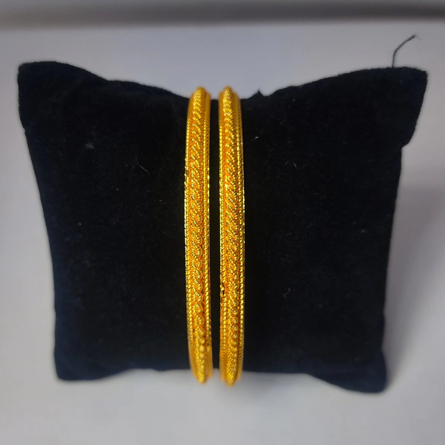 Two gold plated bangles with classic micro texturing on a black cushion with a white background