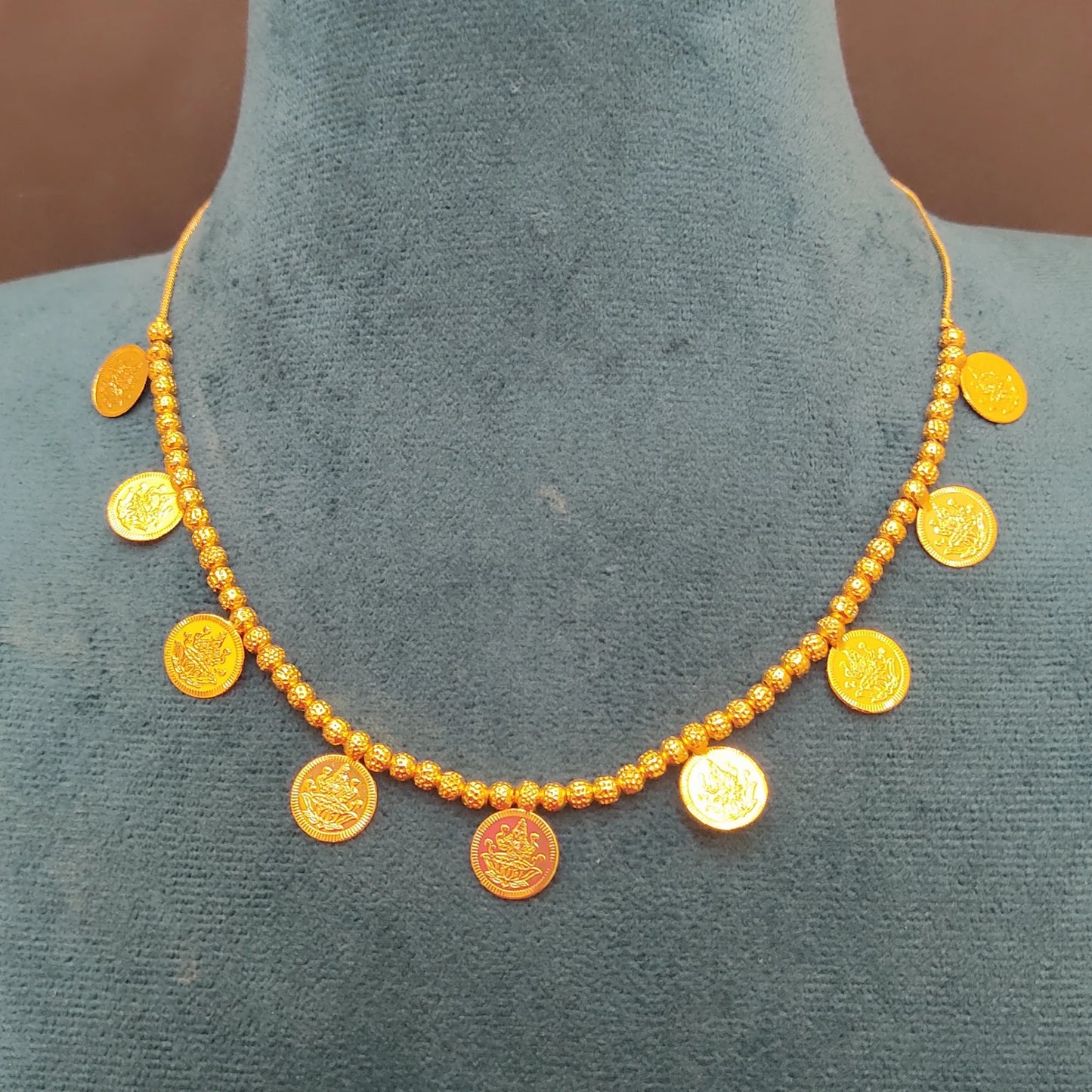Gold plated necklace with lakshmi coin pendants on a mannequin bust.