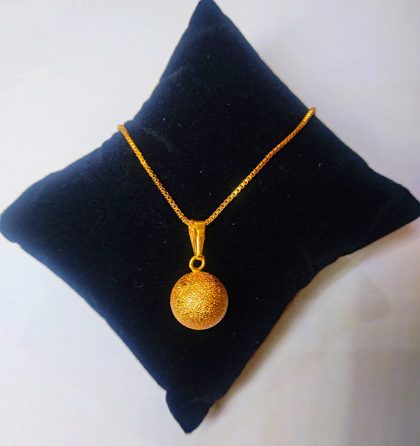 Gold plated necklace with a round pendant on a black cushion