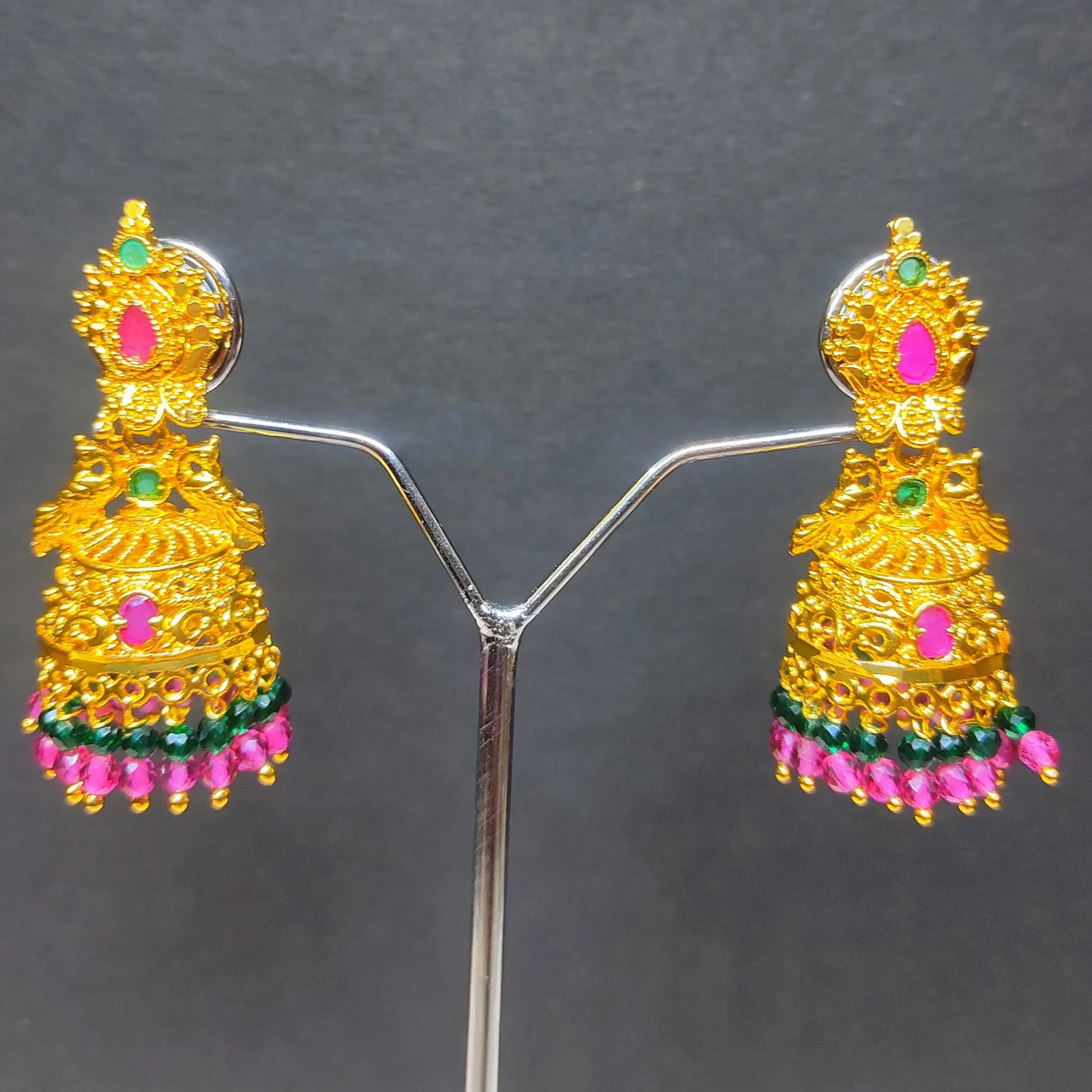 Gold plated Peacock Motif jimikki/Jhumka earrings with pink and green accents on a gray background