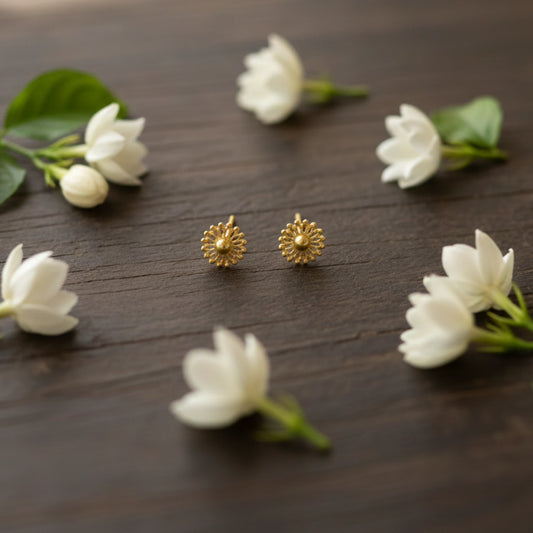 Gold plated sunburst stud earrings on a wooden surface with white flowers and green leaves.