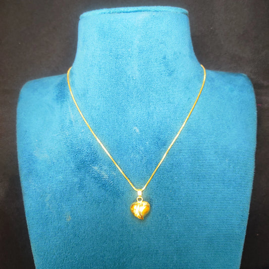 Gold plated heart-shaped pendant necklace on a blue velvet stand with a black background