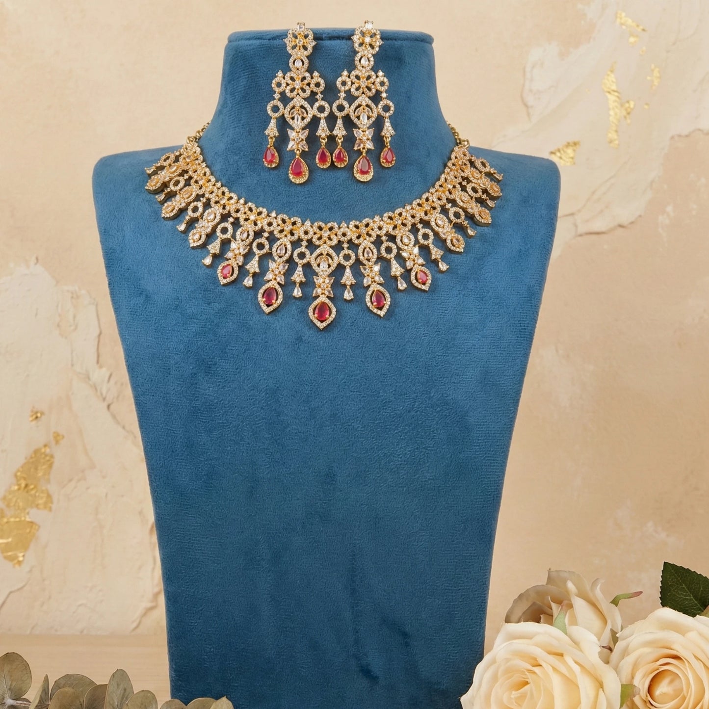 Gold plated Red necklace and earrings set on a blue stand with a floral background