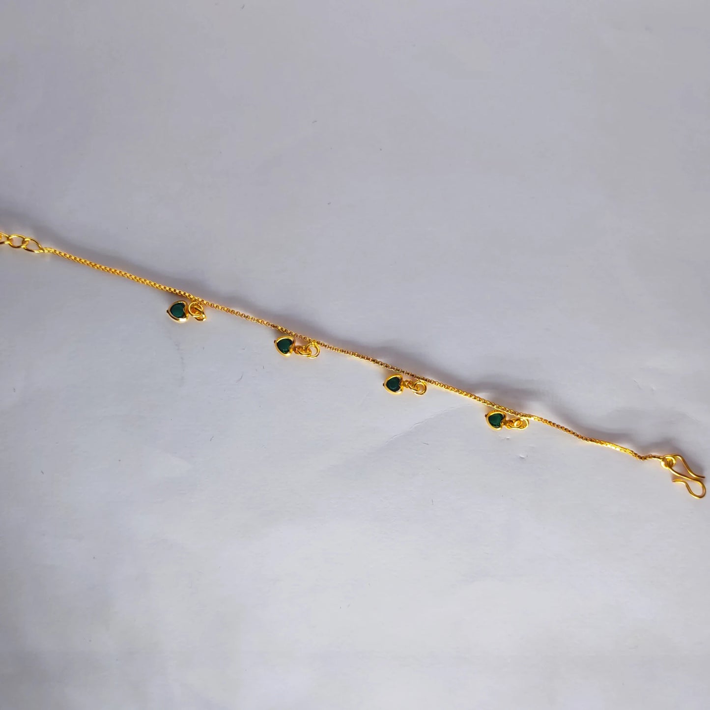 Gold plated bracelet with green heart charm stones on a light gray background