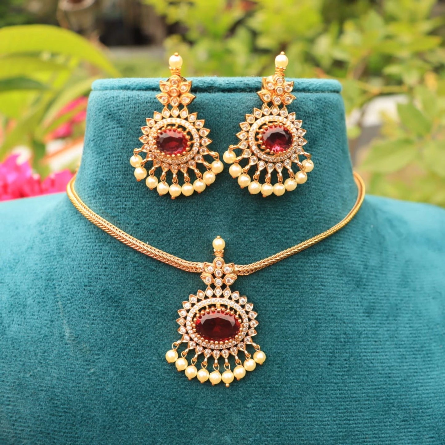 Gold toned necklace and earrings set on a teal mannequin with a blurred natural background