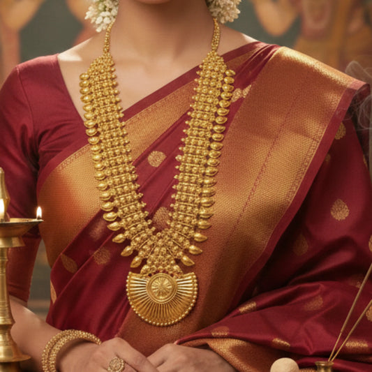 Person wearing a traditional maroon saree with gold plated long haram necklace jewelry