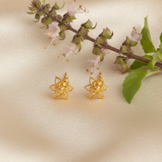 Gold plated small flower-shaped earrings on a beige background with a branch of flowers.