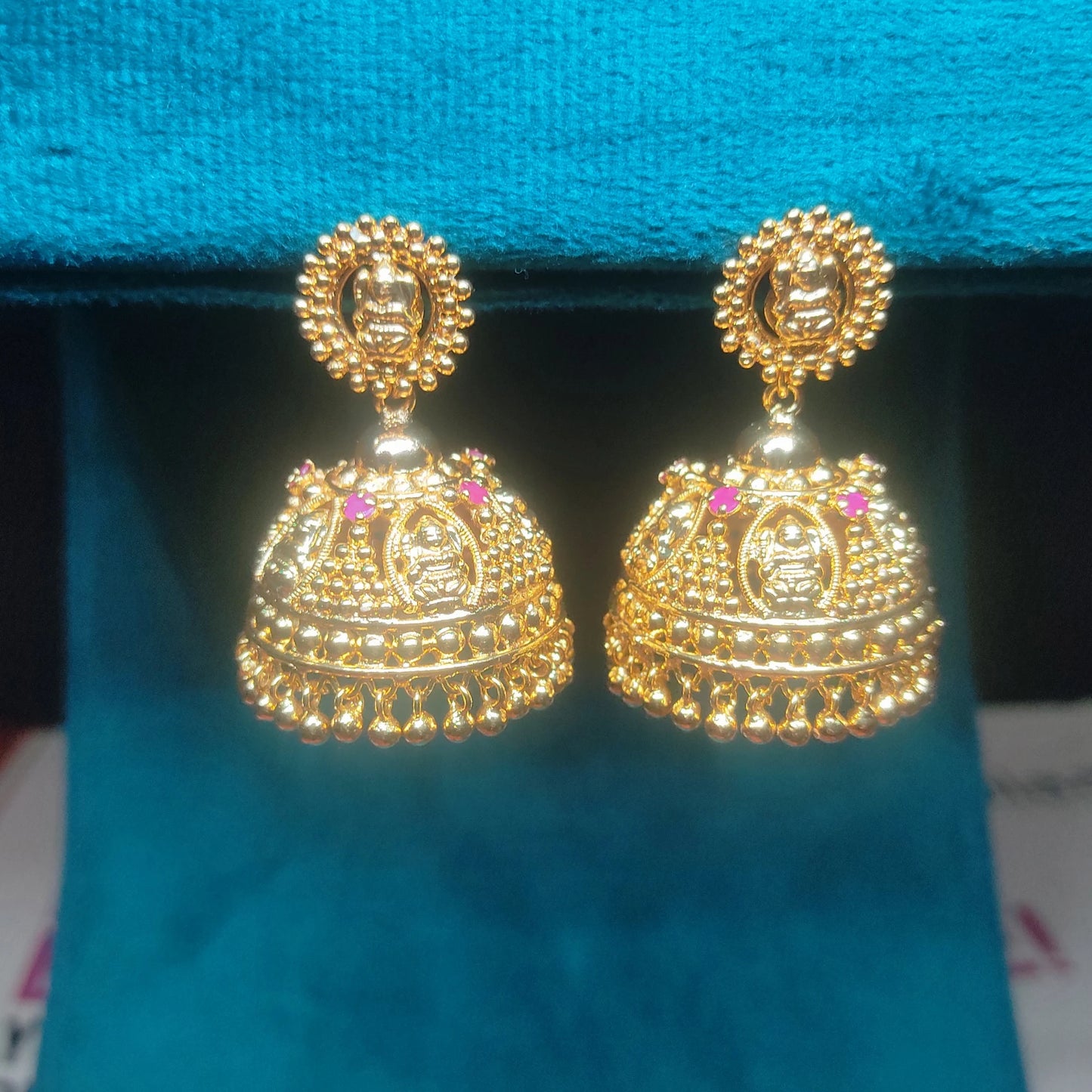 Gold plated traditional Lakshmi heritage Jimikki/Jhumka earrings with pink stones on a blue background