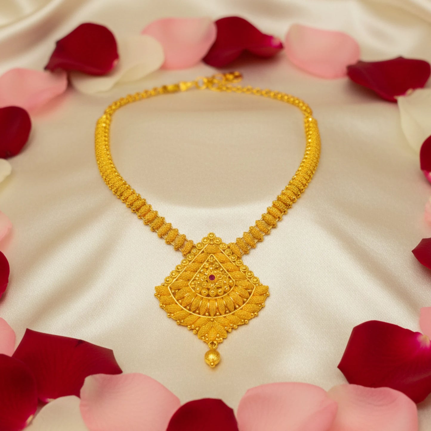 Gold plated long haram necklace with intricate design on a white fabric background with red and pink rose petals.