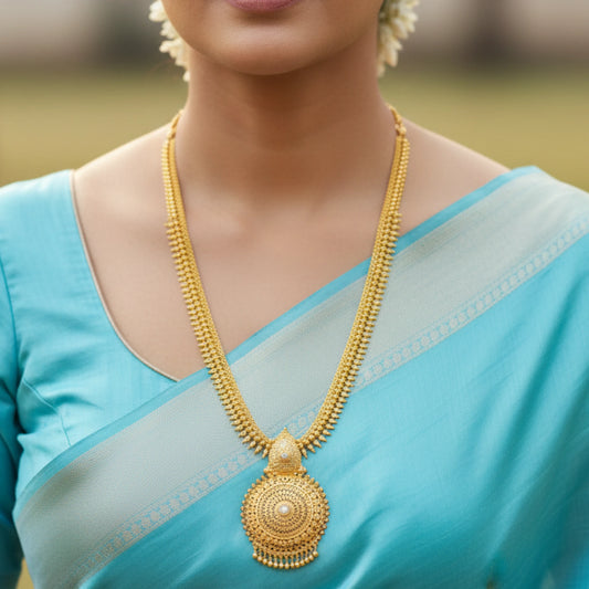 Woman wearing a blue saree with a gold plated long haram necklace with a mandala pendant