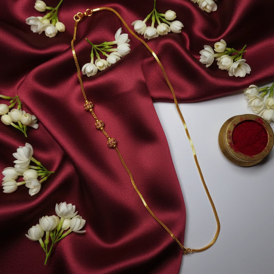 Gold plated mugappu chain with red stones on a red fabric background with white flowers