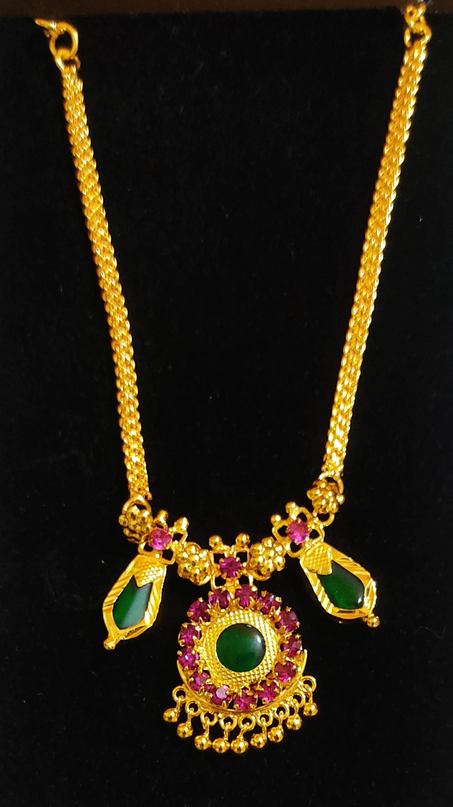 Gold plated choker necklace with green nagapadam and a pendant with ruby red gemstones on a black background