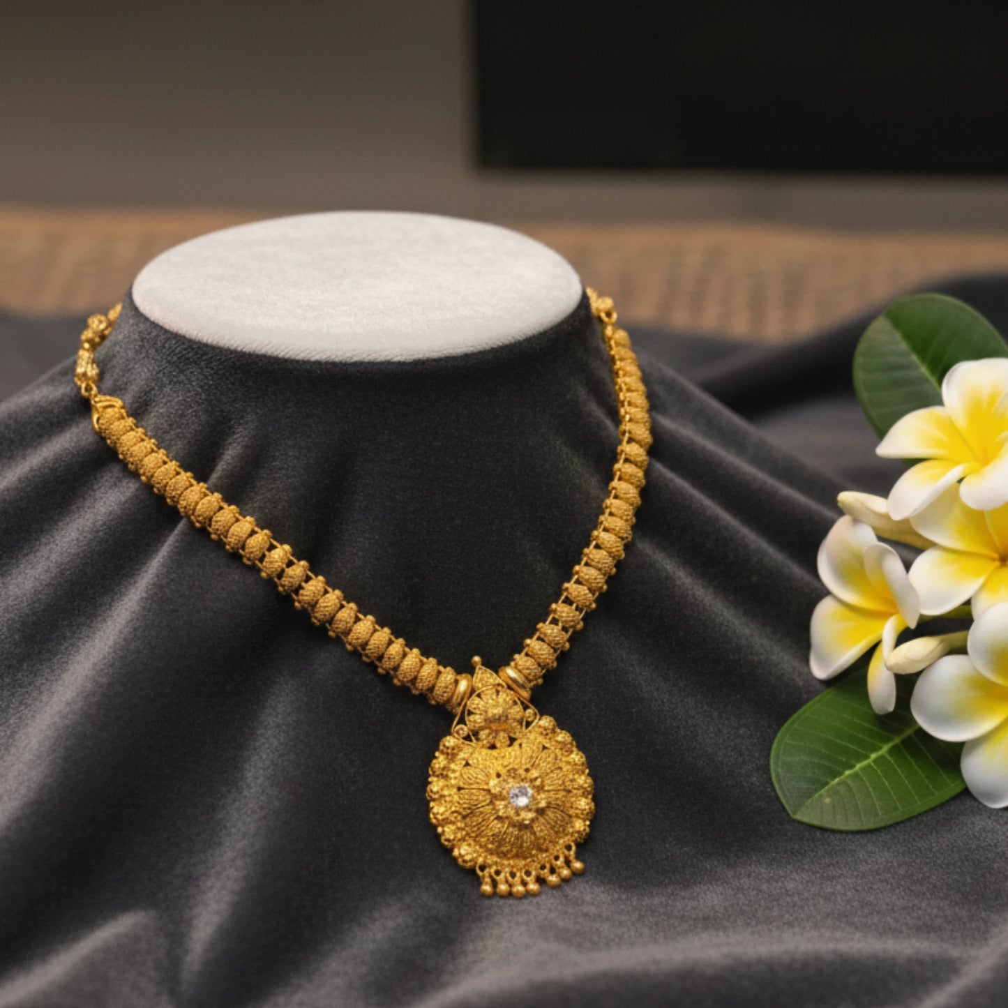 Gold plated necklace with a floral mandala pendant with a beaded chain on a mannequin bust with flowers on a dark fabric background