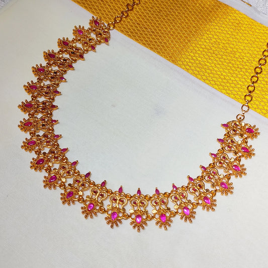 Gold plated traditional choker necklace with pink gemstones on a white and yellow fabric background