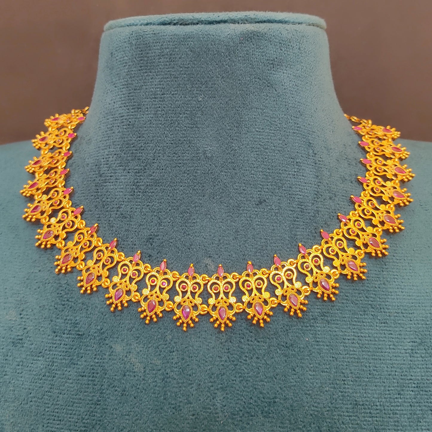 Gold plated traditional ruby choker necklace with pink stones on a green mannequin bust